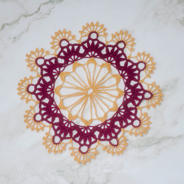 Doily in three layer colors: yellow center, burgundy middle, yellow outer. The center fans out like a ferris wheel into twelve points, the middle takes each point and attaches  containers to the spokes that themselves hold five smaller points, like people together. Each container there is topped with a circle from which the outer layer attaches, crowning each segment with nine-spoke fans each. Set against a white marbled background.